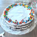 An ice cream cake topped with whipped cream, and mini colorful m&m's candies.