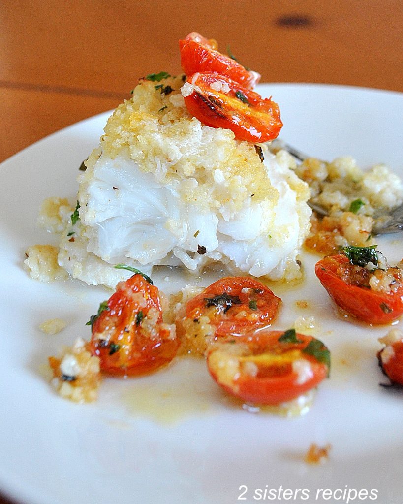 Piece of cod with sliced tomatoes on white plate.