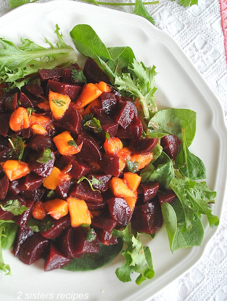 A white plate with lettuce, chopped beets and mango on it.   by 2sistersrecipes.com