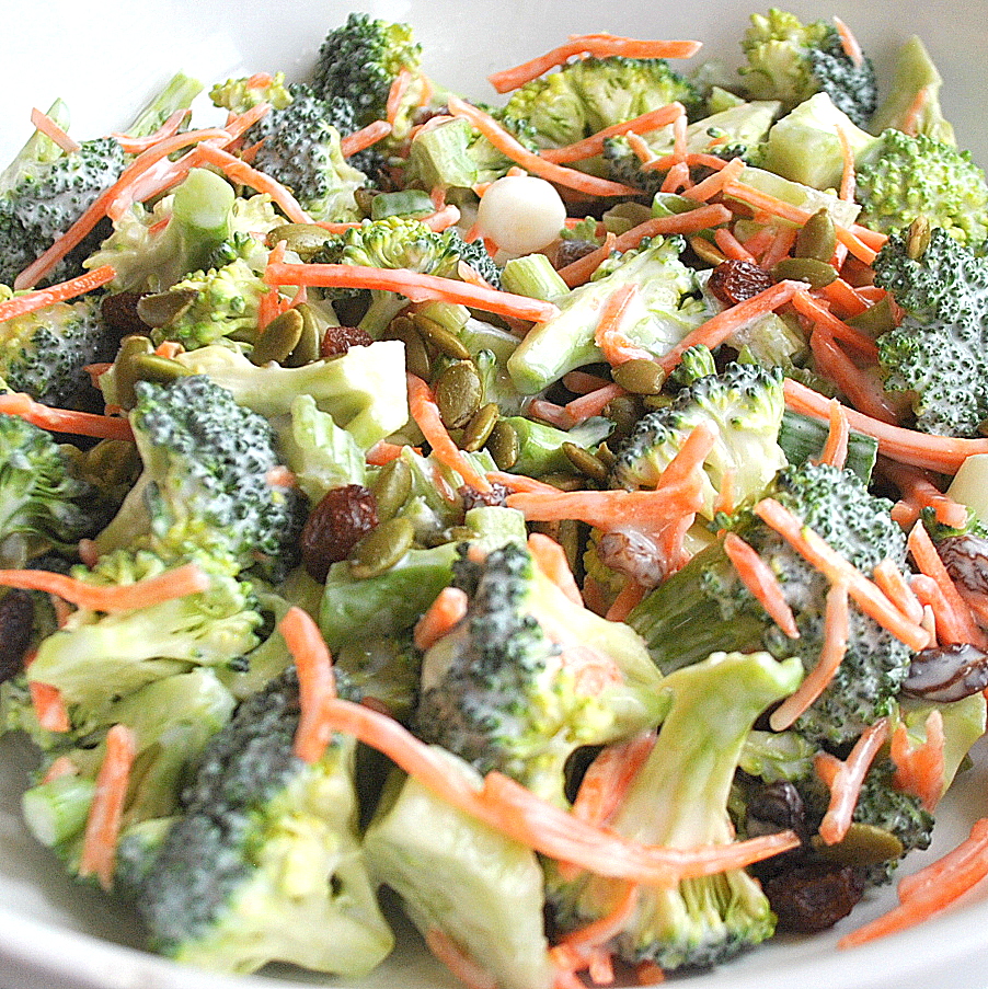 A white salad bowl with chopped broccoli florets, shredded carrots and raisins. salad.