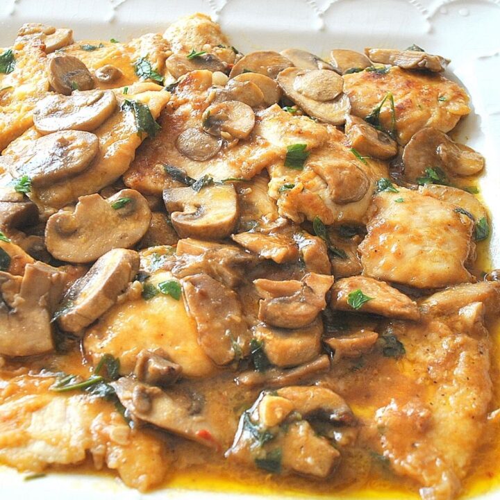 A white platter filled with pieces of cooked chicken smothered in a marsala wine sauce.