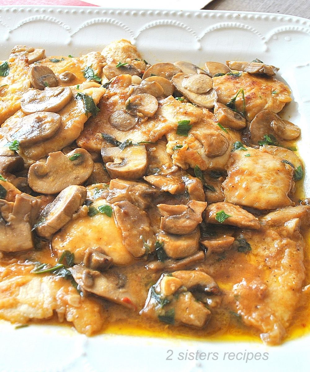 A white platter filled with pieces of cooked chicken smothered in a marsala wine sauce.