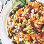 A large white bowl filled with a mixture of beans and veggies tossed in a dressing and served as a salad.