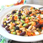 A white bowl loaded with Mediterranean Bean Salad loaded with chopped veggies.