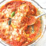 A spoonful of ravioli covered with tomato sauce and cheese.