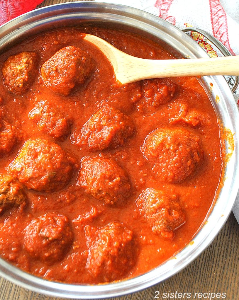 A pot filled with meatballs sitting in tomato sauce. by 2sistersrecipes.com