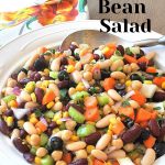 A white bowl filled with mixture of beans and veggies with a serving spoon.