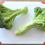 Fresh heads of fresh broccoli placed on a white and red cutting board.