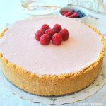 An entire raspberry cheesecake with fresh raspberries on top and crumb crust around the edges.