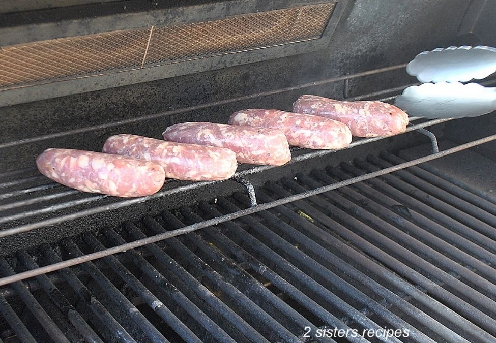 raw sausages placed on the top rack of the grill. by 2sistersrecipes.com