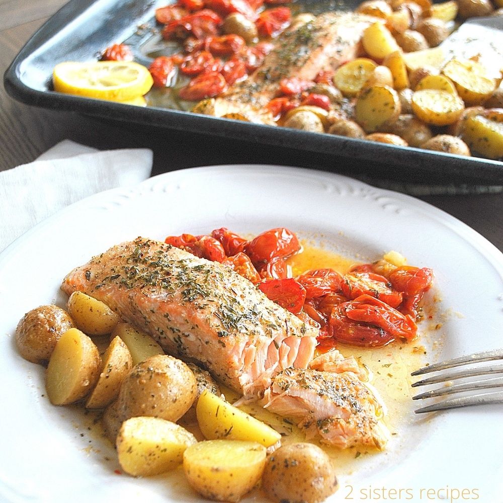 A white dinner plate with cooked salmon, small potatoes and cherry tomatoes. 