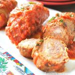A platter filled with rolled meats stuffed with cheese and prosciutto smothered with tomato sauce.