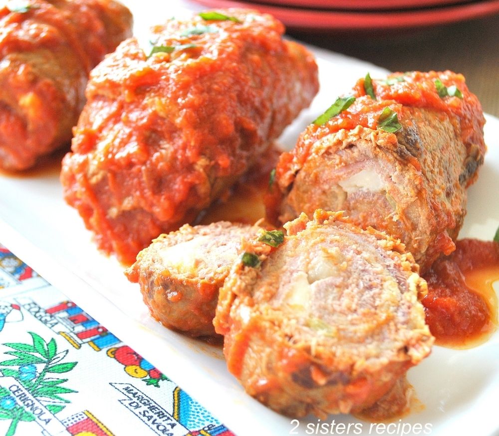 A platter filled with rolled meats stuffed with cheese and prosciutto smothered with tomato sauce.