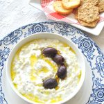 A bowl of white creamy Tzatziki sauce with a few olives on top.
