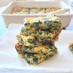 Squares of baked eggs, cheese and spinach piled on top on a parchment paper.