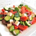 White square plate filled with chopped cucumbers, tomatoes, red onion and cubed of feta cheese.