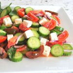 A white plate filled with chopped cucumbers, tomatoes, red onion and cubes of feta cheese.