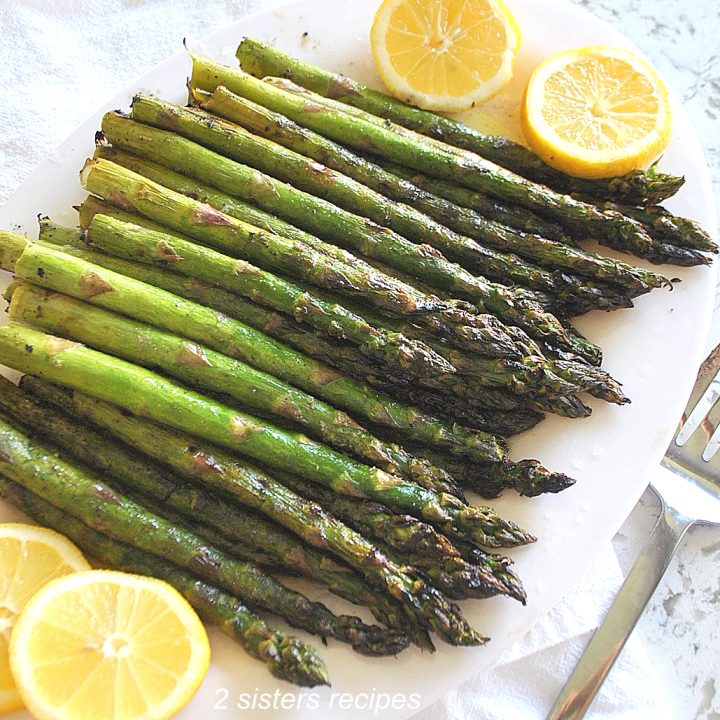 A bunch of grilled asparagus served on a white platter with lemon wedges on the sides.