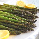 A white plate with grilled asparagus and lemon wedges.