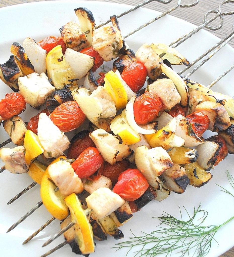 A white platter with swordfish and veggies kabobs grilled.