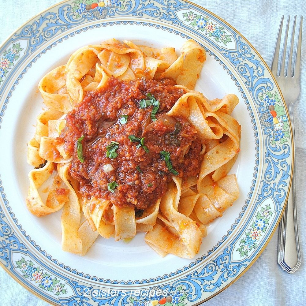 A blue plate filled with pappardelle pasta with tomato sauce on top. 