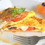 An omelet stuffed with tomato and melted mozzarella with a fork on a white plate.