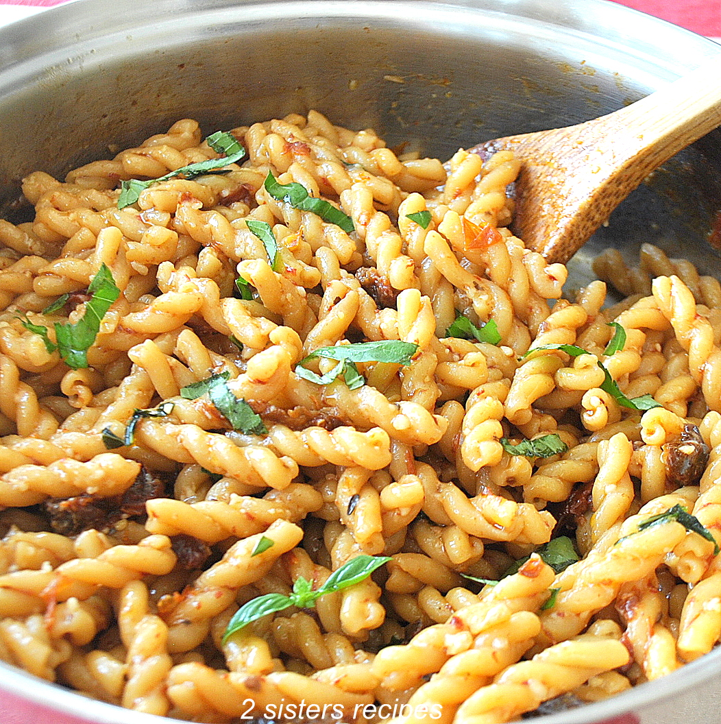 A large silver skillet filled with cooked curly pasta, ribbons of basil, and a wooden spoon.