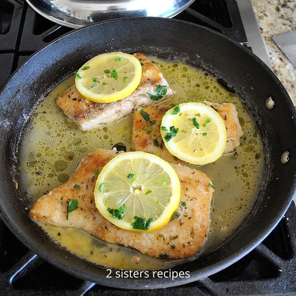 A black skillet with cooked mahi and lemon sliced on top. by 2sistersrecipes.com