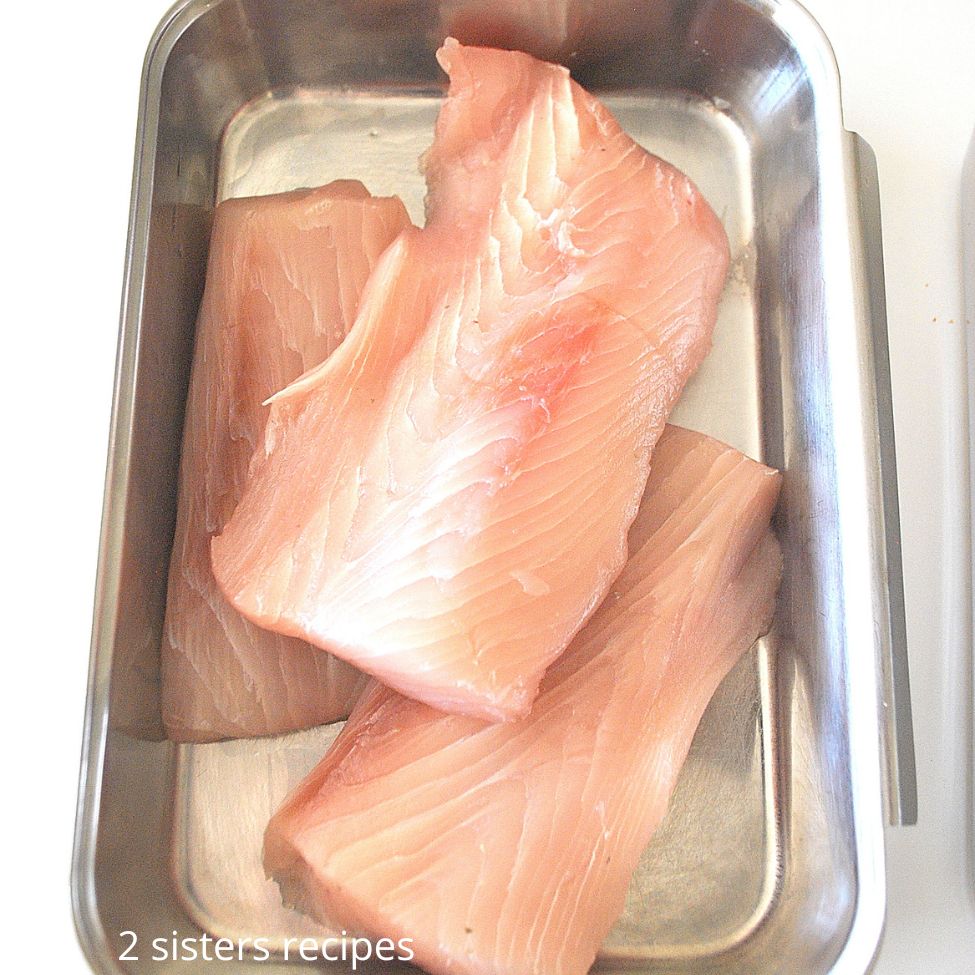 Raw filets of mahi in a stainless steel pan. by 2sistersrecipes.com