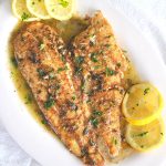Cooked filet of sole in a lemon sauce on the serving platter, with lemon slices on the side.