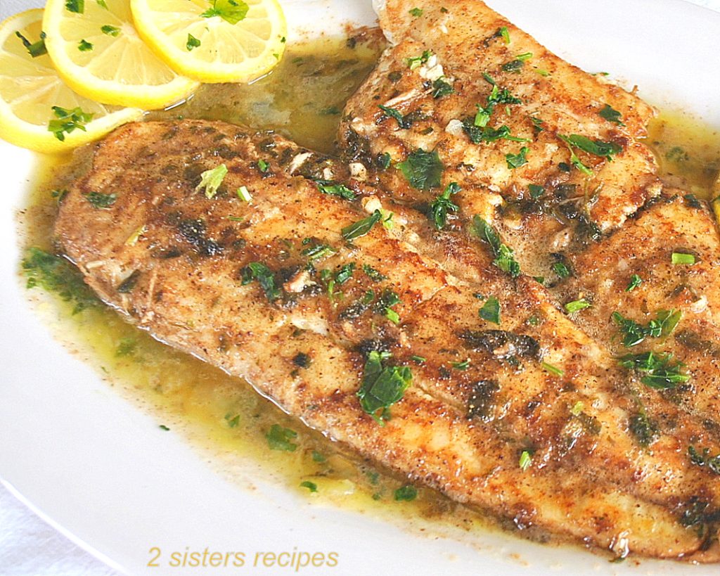 A large piece of cooked fish with lemon sauce on a white platter.