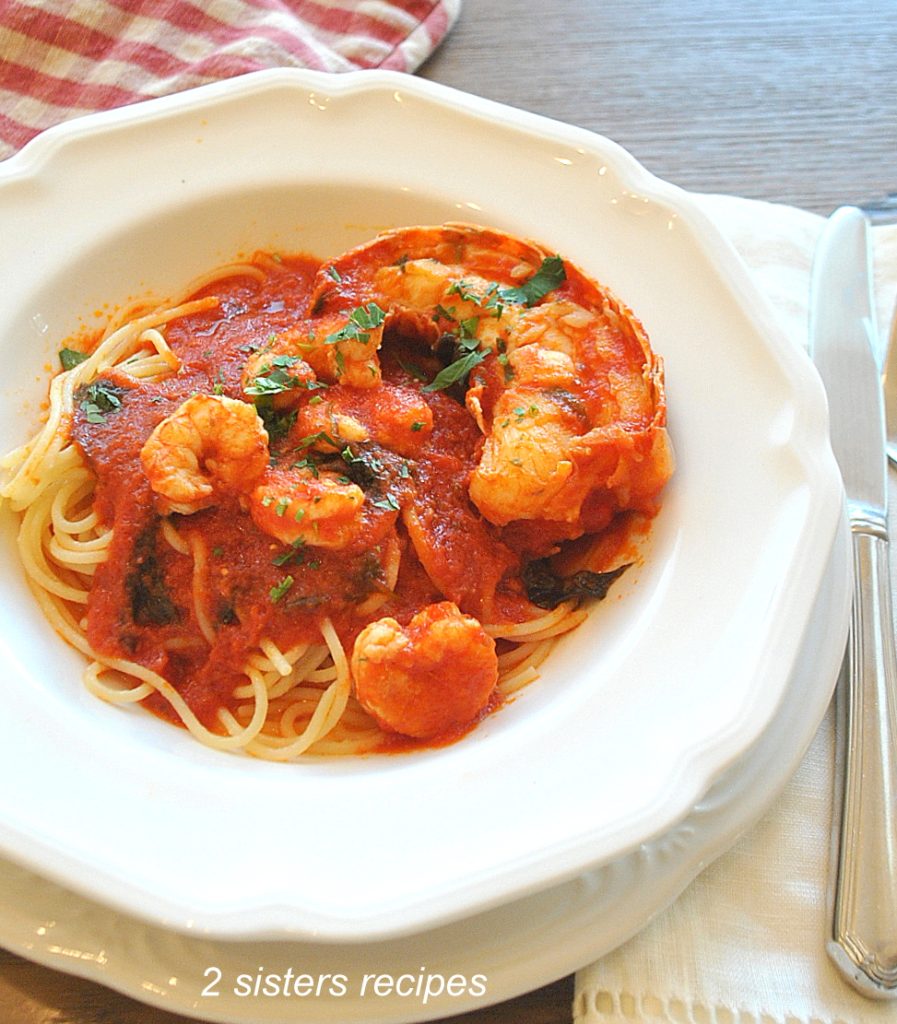 A white dinner plate with a serving of spaghetti and seafood red sauce. by 2sistersrecipes.com