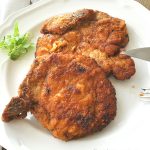 On a white dinner plate, two fried pork chops.