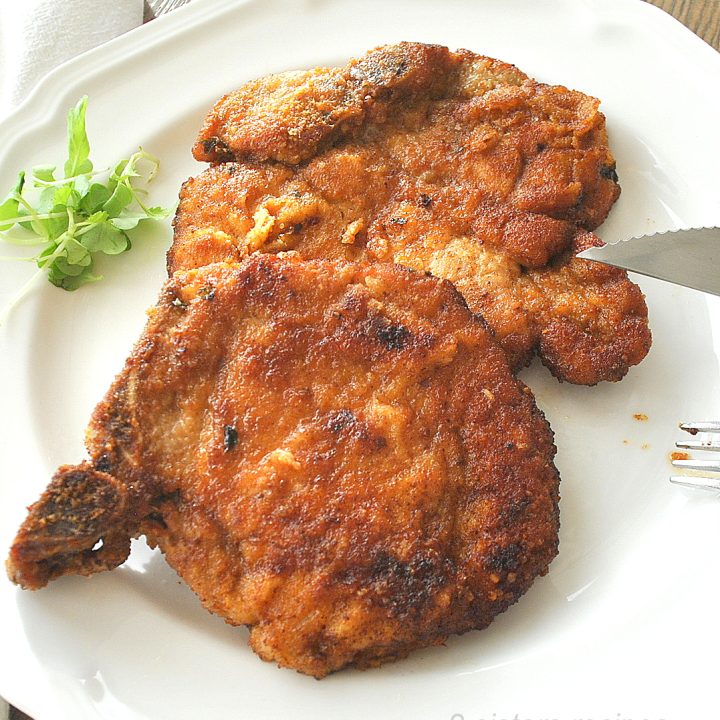 On a white dinner plate, two fried pork chops.