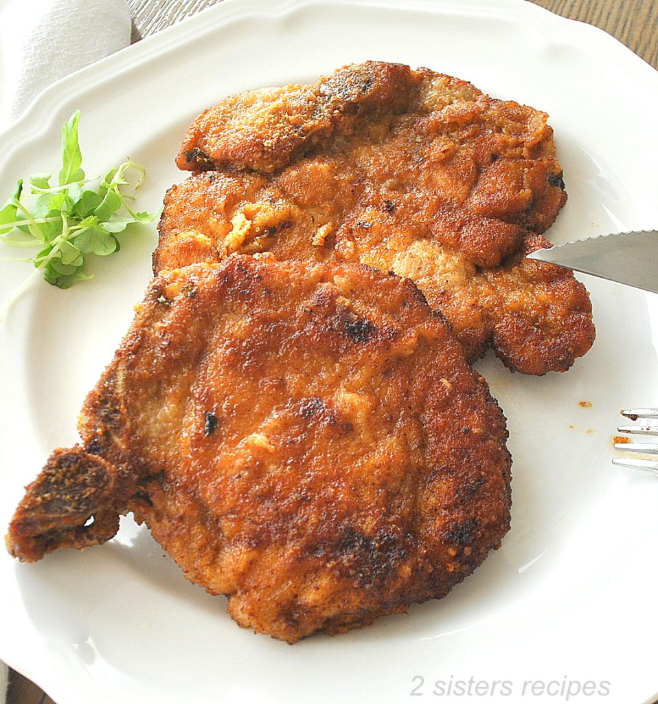 On a white dinner plate, two fried pork chops.