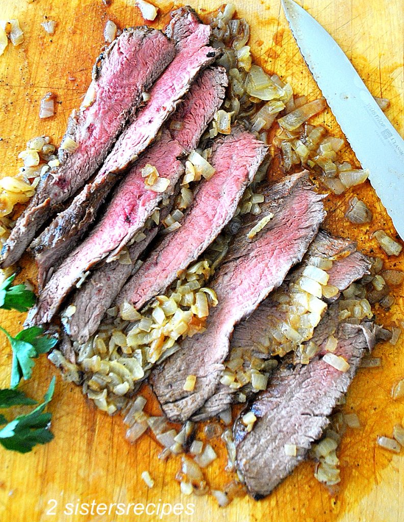 Sliced steak on a wooden cutting board. by 2sistersrecipes.com
