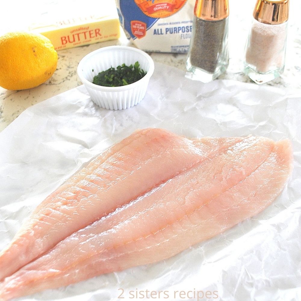 Raw filet of fish on wax paper with ingredients nearby. by 2sistersrecipes.com