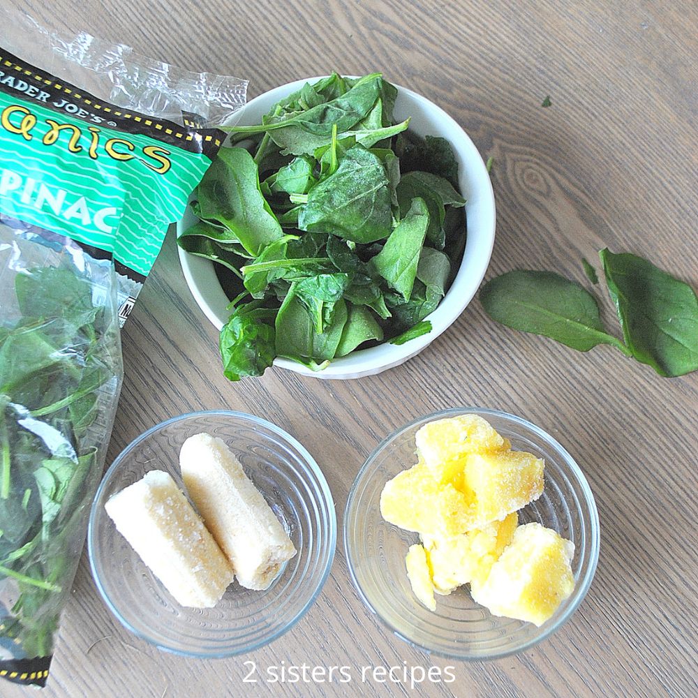 The 3 main ingredients, frozen spinach, banana, and chunks of pineapple in glass bowls on the table. 