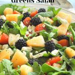 A large white salad bowl filled with chopped cantaloupe, fresh blackberries and feta cheese with mixed greens as a salad.