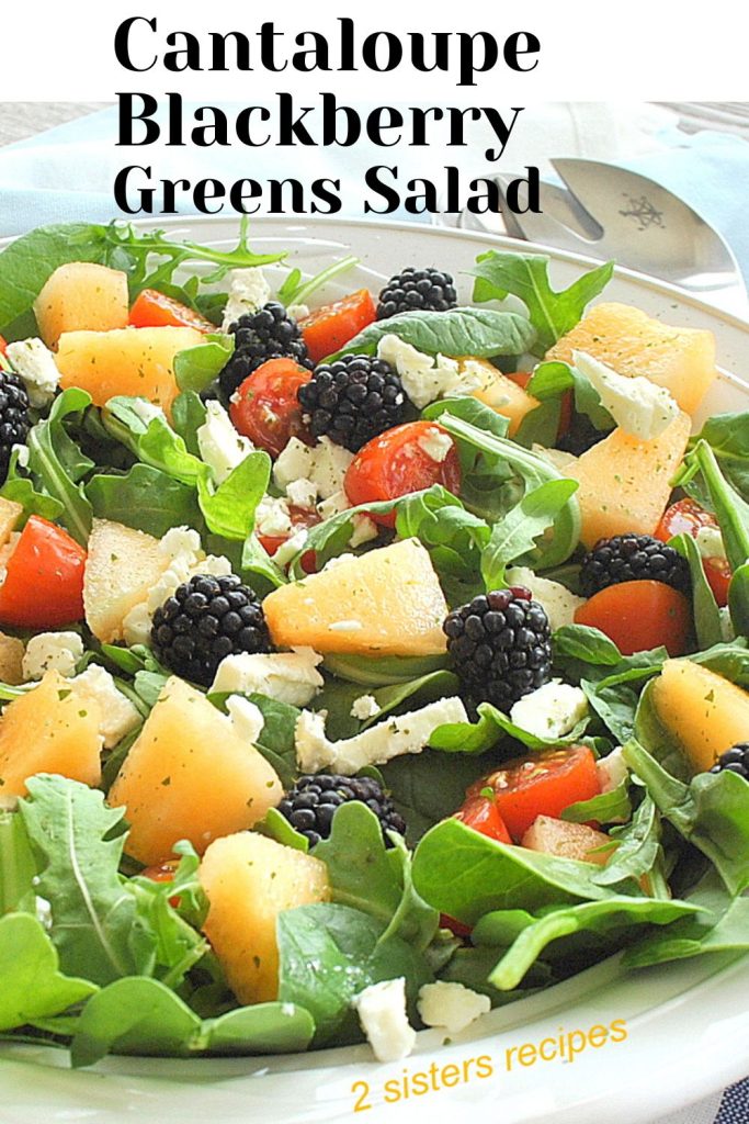 A large white salad bowl filled with chopped cantaloupe, fresh blackberries and  feta cheese with mixed greens as a salad.