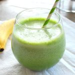 A spinach smoothie in a short glass with a green and white stripe straw in it.