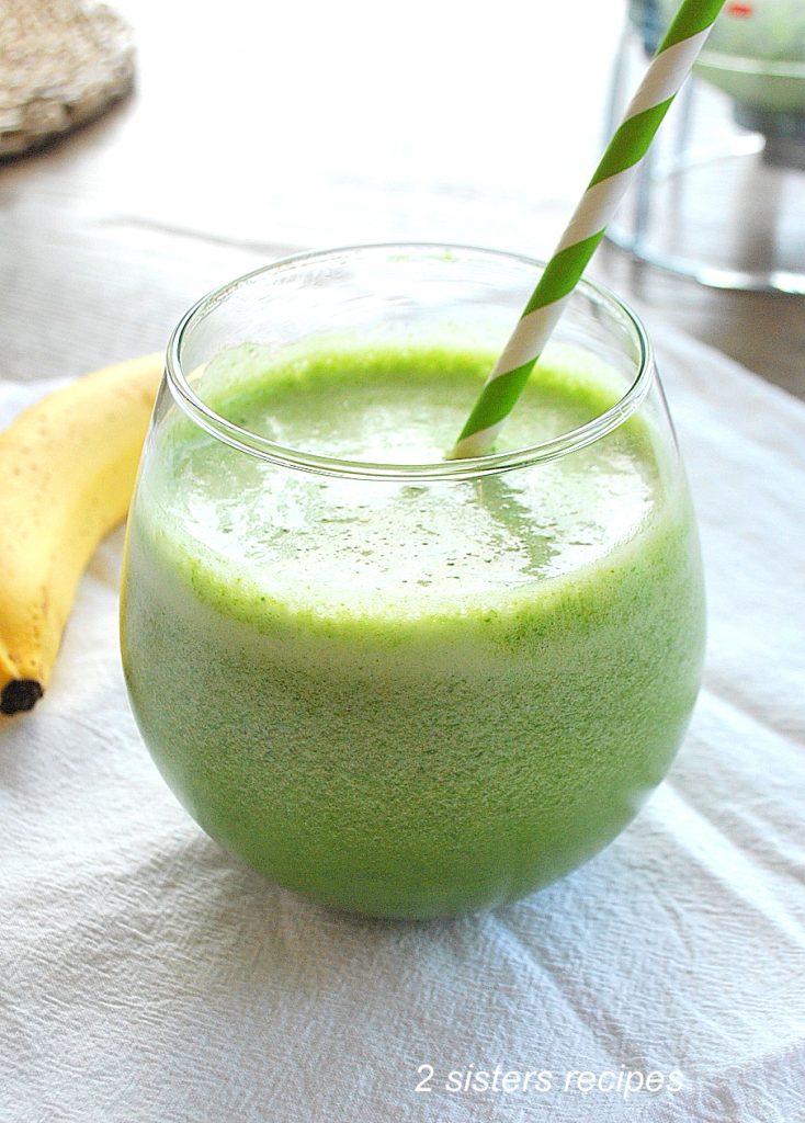 A spinach smoothie in a short glass with a green and white stripe straw in it.