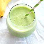 A Spinach Smoothie served in a round short glass with a green and white stripe straw.