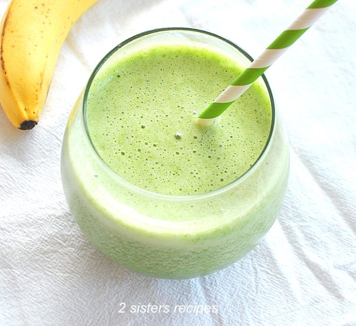 A Spinach Smoothie served in a round short glass with a green and white stripe straw.