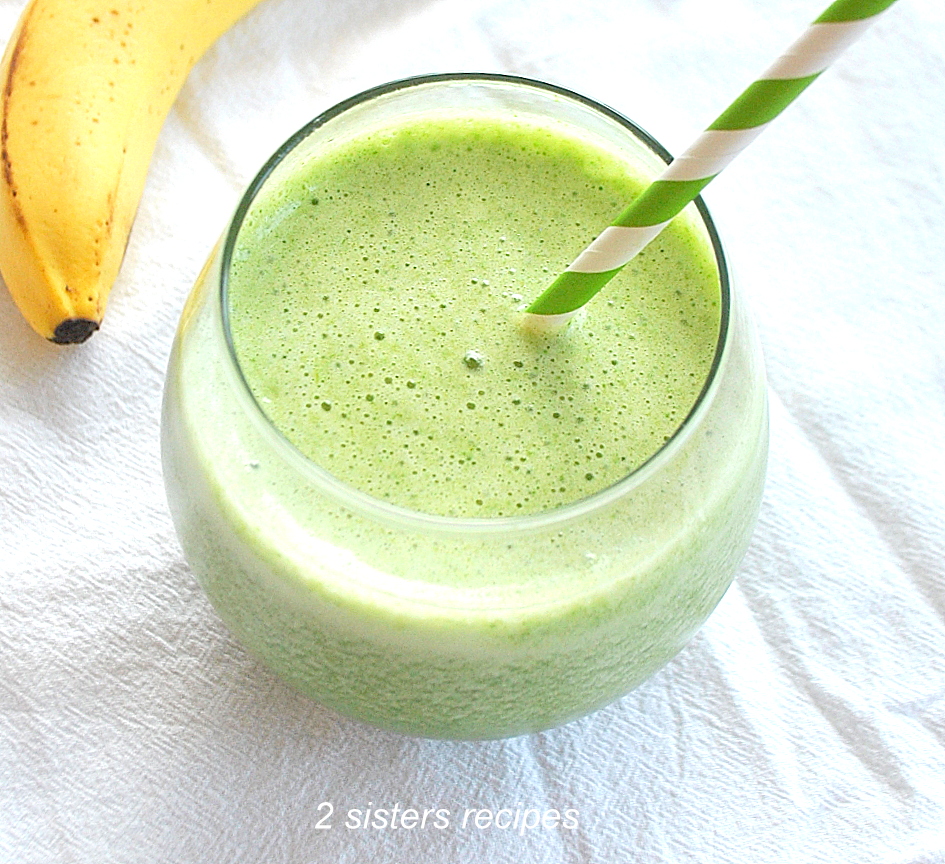 A Spinach Smoothie served in a round short glass with a green and white stripe straw.