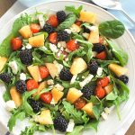 A large white salad bowl with blackberries, cantaloupe, feta cheese and fresh greens.