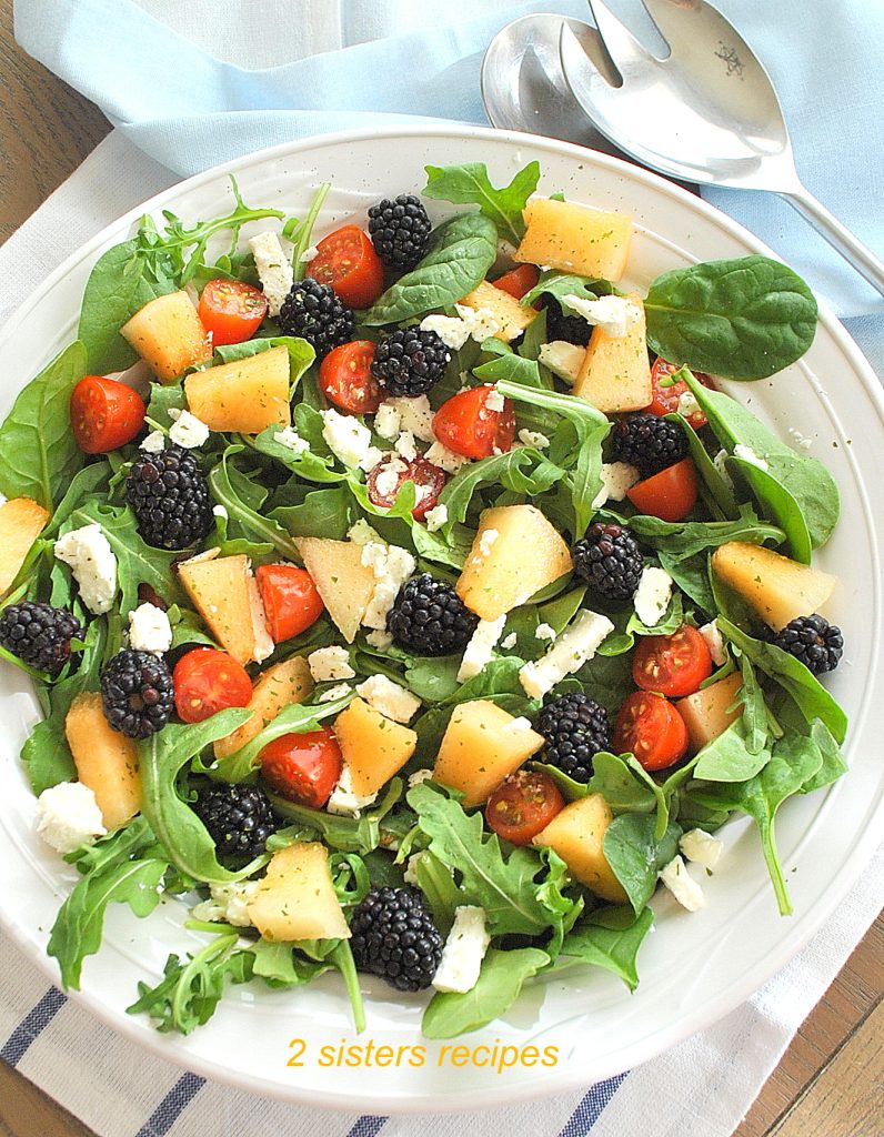 A white bowl with blackberries, cantaloupe, feta cheese and fresh greens. by 2sistersrecipes.com
