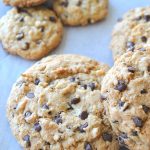 Large size cookies alongside the smaller size chocolate chip cookies on a sheet of wax paper.