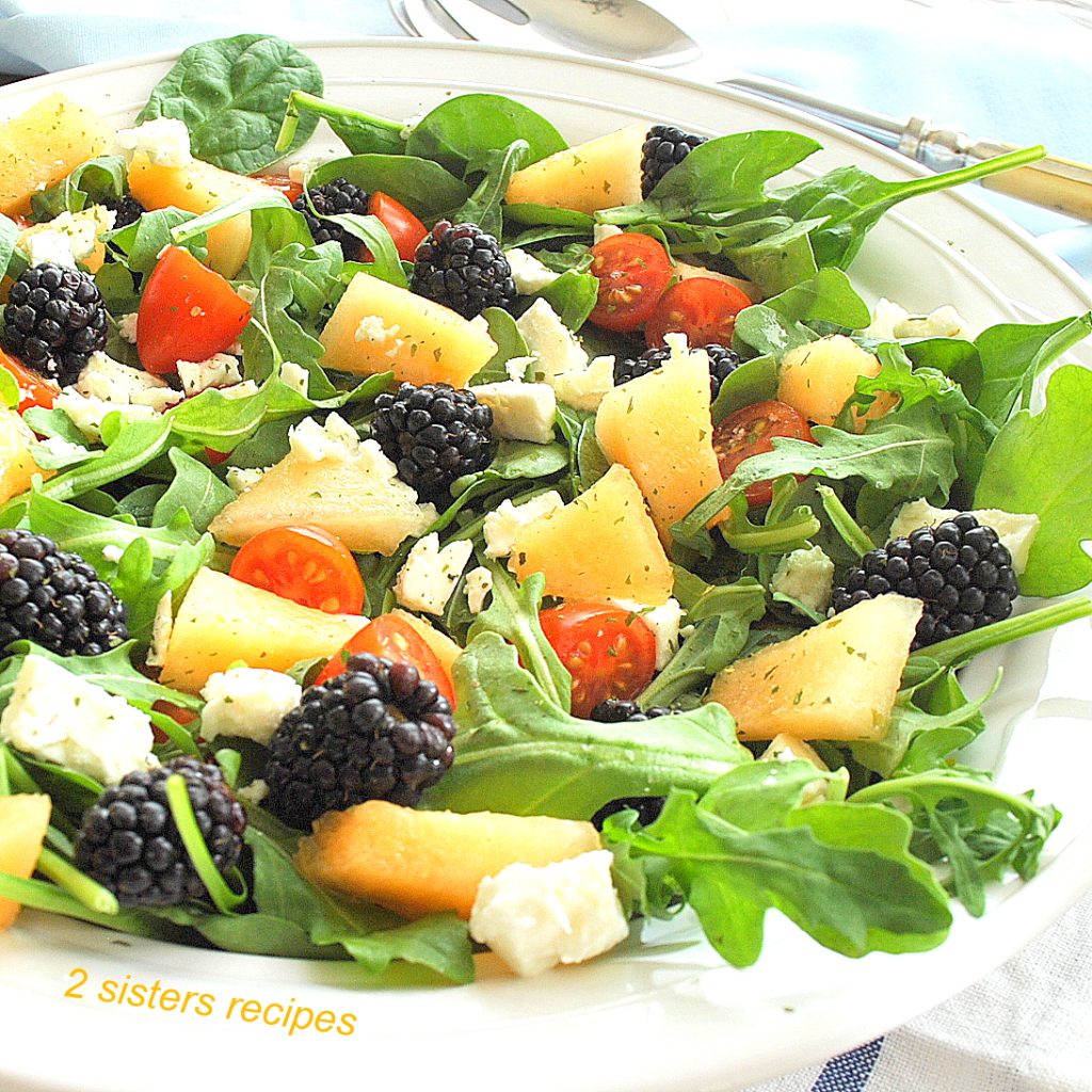Fruit and cherry tomatoes and feta cheese scattered over a bed of greens. by 2sistersrecipes.com