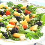 Fruit and cherry tomatoes and feta cheese scattered over a bed of greens.